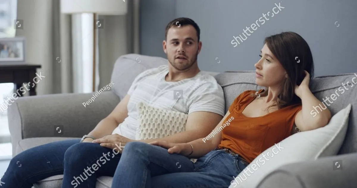 Young couple sitting apart on a gray sofa, the woman looking away