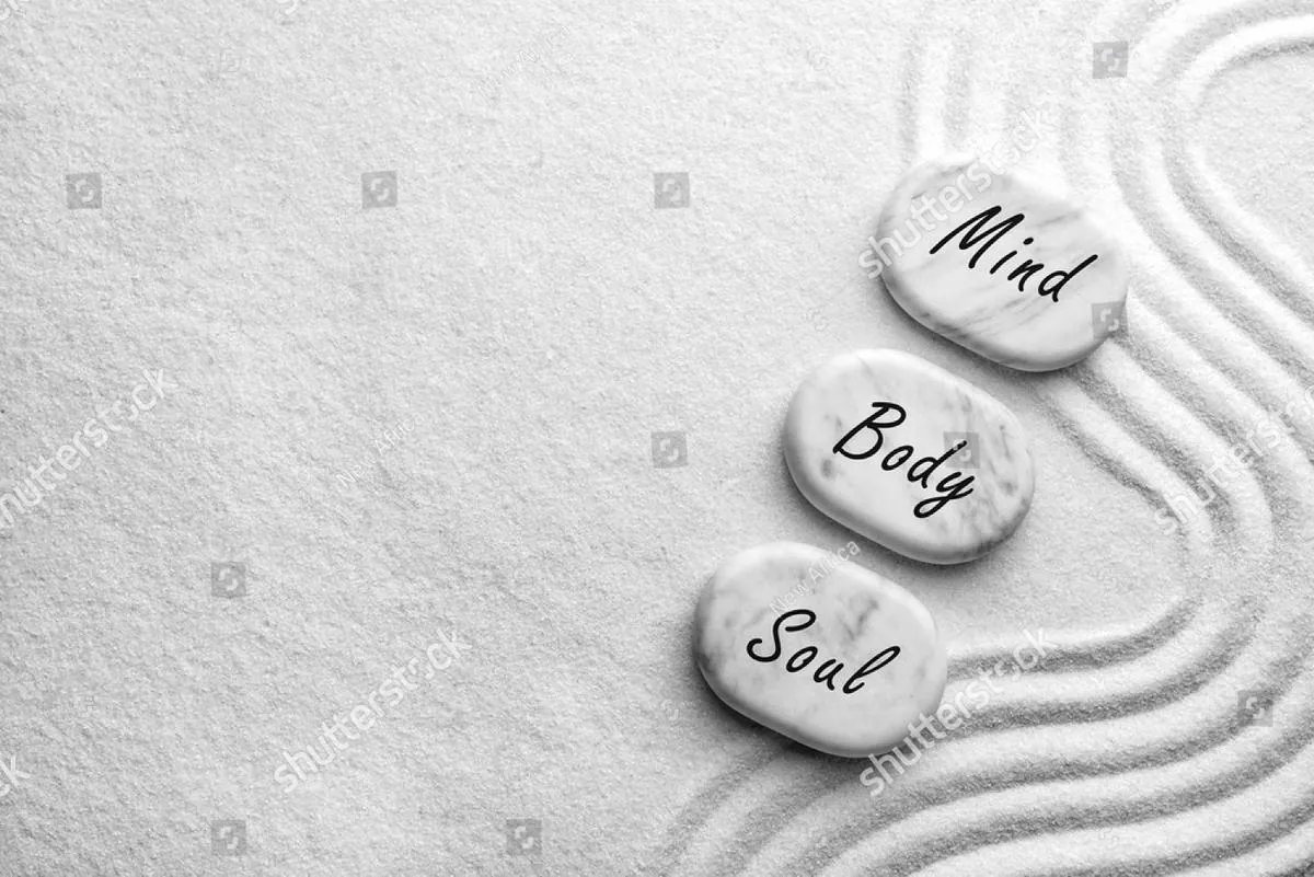 Three white stones labeled Mind, Body and Soul on raked sand