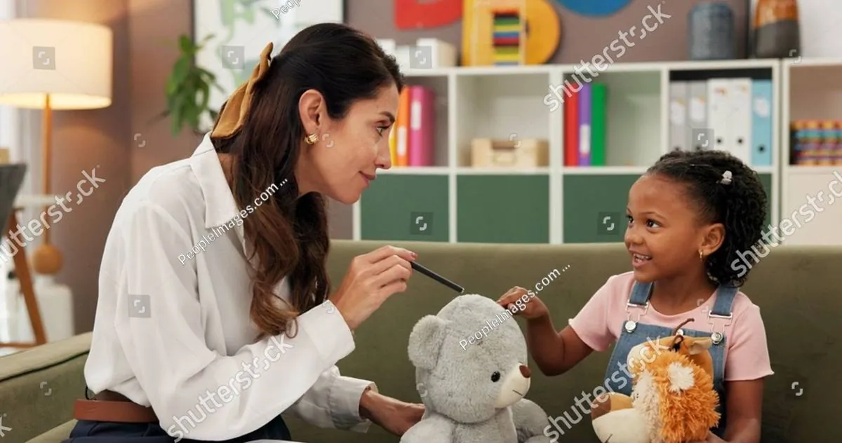 A therapist talks with a smiling young girl holding stuffed animals on a sofa