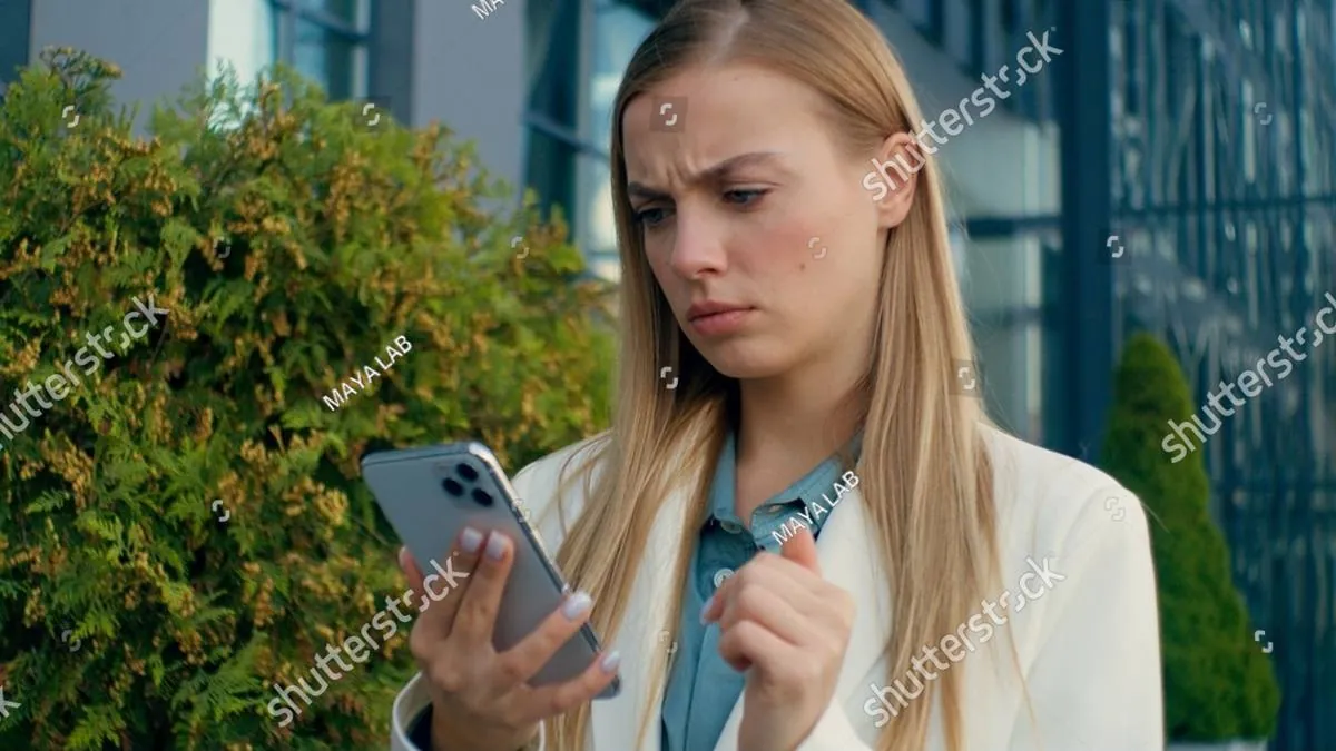 Woman in a white blazer frowning at her phone outside an office building