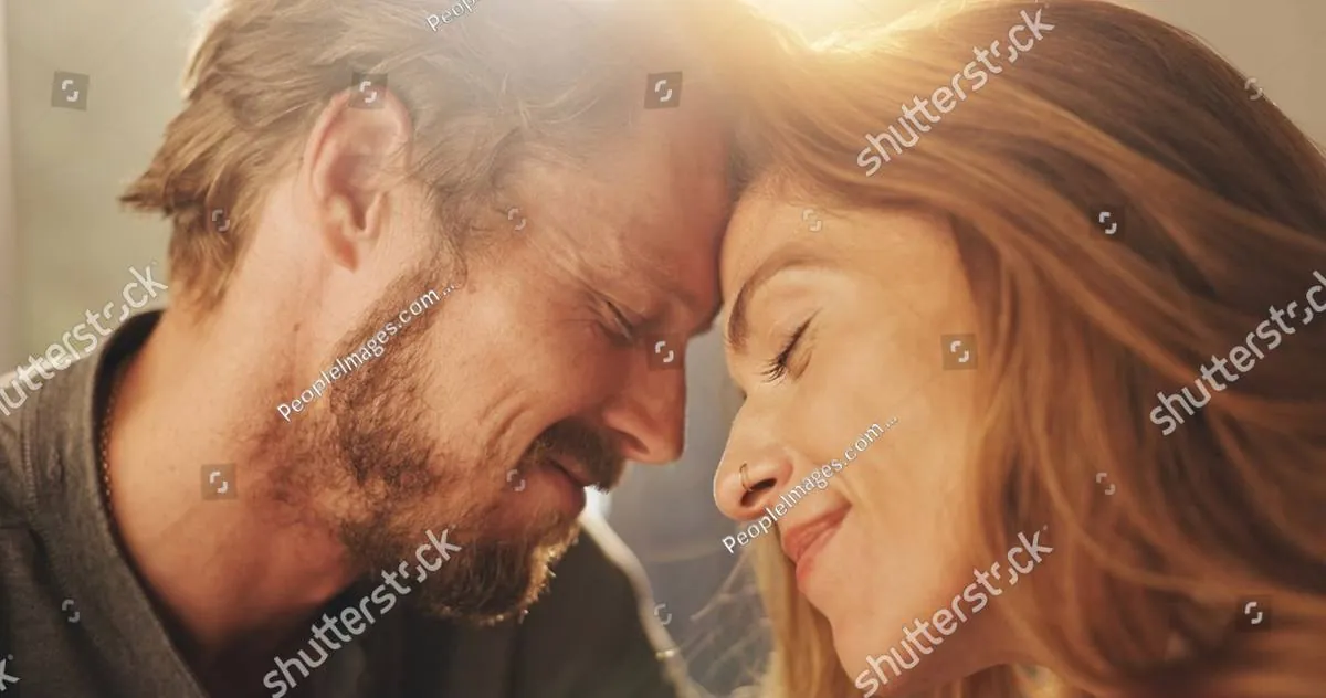 A smiling couple rests their foreheads together in warm golden sunlight