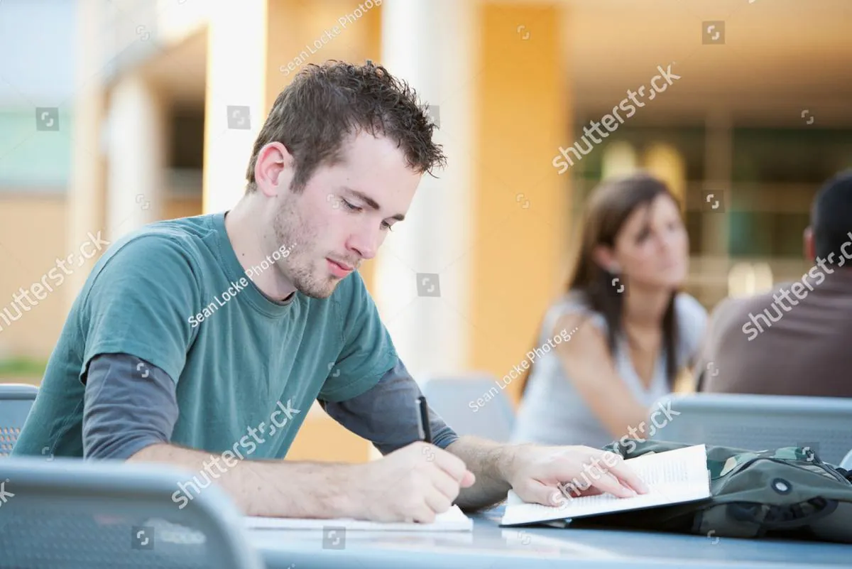 Young man writing in a notebook at an outdoor campus table
