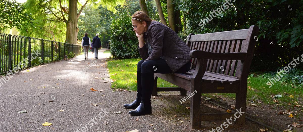 Woman sitting alone on a park bench with her chin in her hand