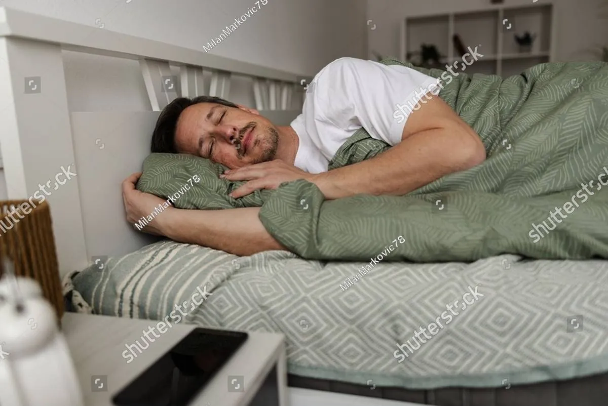 A man sleeps peacefully in bed under a green blanket