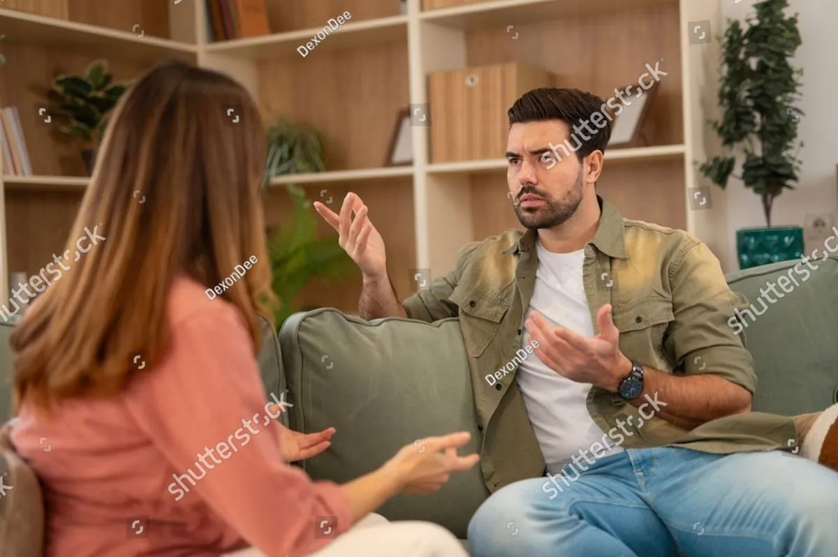 A man on a green sofa gestures while talking with a woman seated across from him