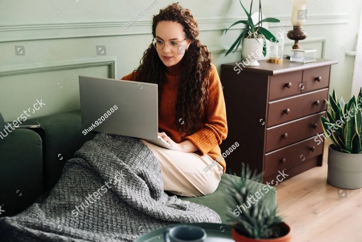 Young woman in an orange sweater working on a laptop on the sofa