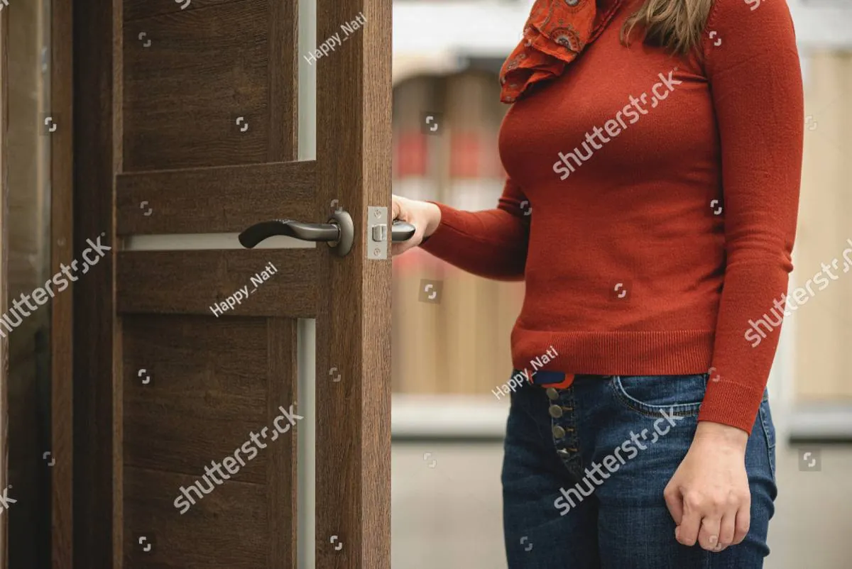 Woman in a rust-colored sweater opening a wooden door by its handle