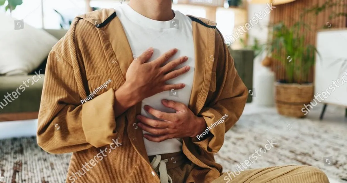 Person in a corduroy jacket sitting on a rug with hands on chest