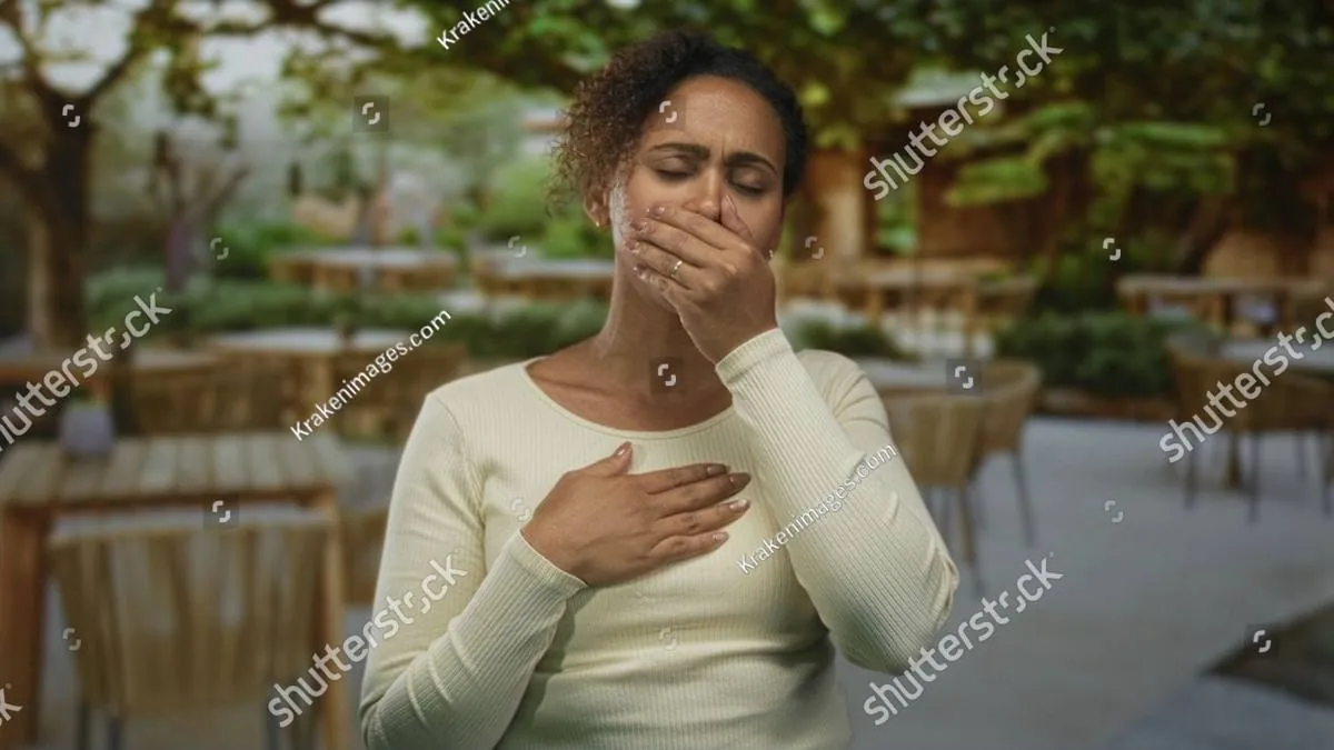 Woman covering her mouth and pressing a hand to her chest at an outdoor cafe