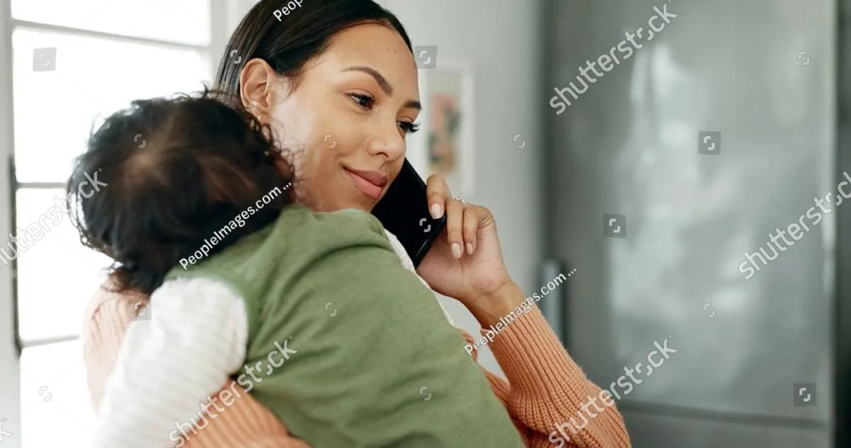 Mother holding her baby on her shoulder while smiling and talking on the phone